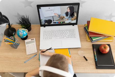Child attending an online class on a laptop with study materials on the desk.
