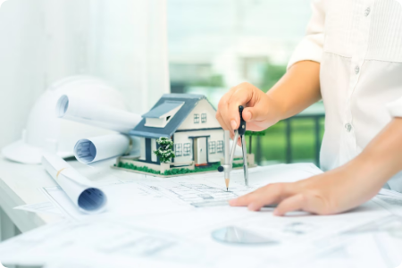 Architect drawing building plans next to a house model.