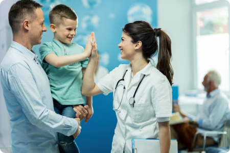 Doctor high-fiving a happy child held by a parent in a clinic.