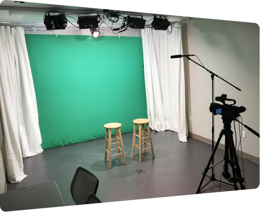 Empty green screen video studio with stools and camera.