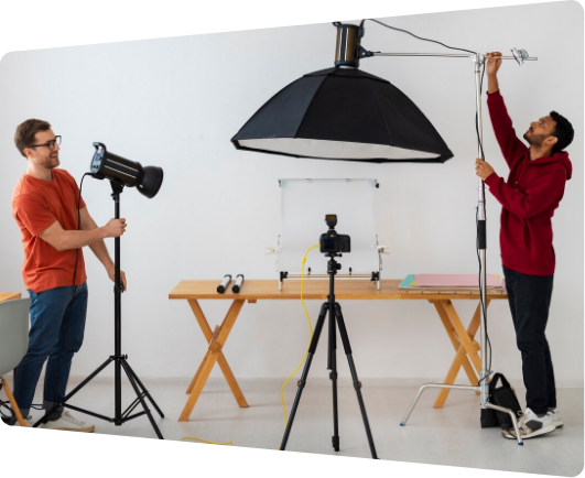 Two men adjusting lighting and camera equipment in a studio